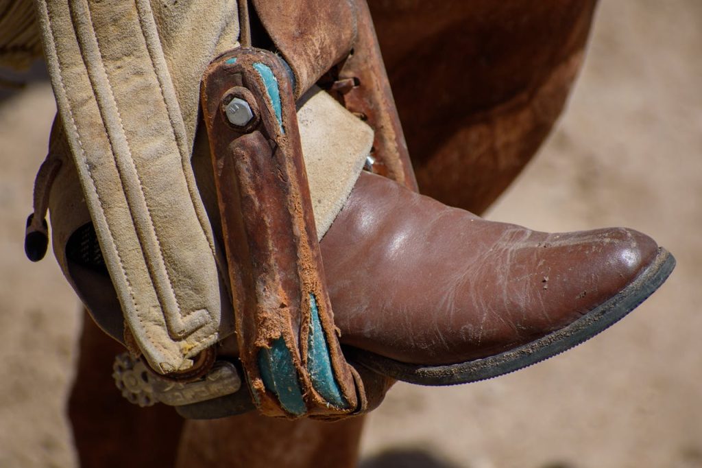 Close-up of a traditional Mexican cowboy boot in a stirrup during an outdoor charrería event.
